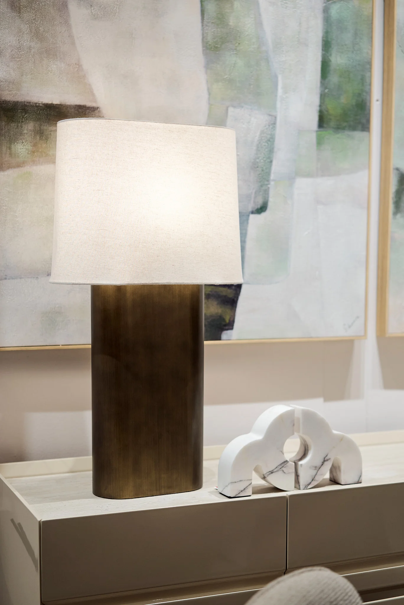 Lámpara de mesa contemporánea con base metálica y pantalla de lino junto a una escultura de mármol blanco.